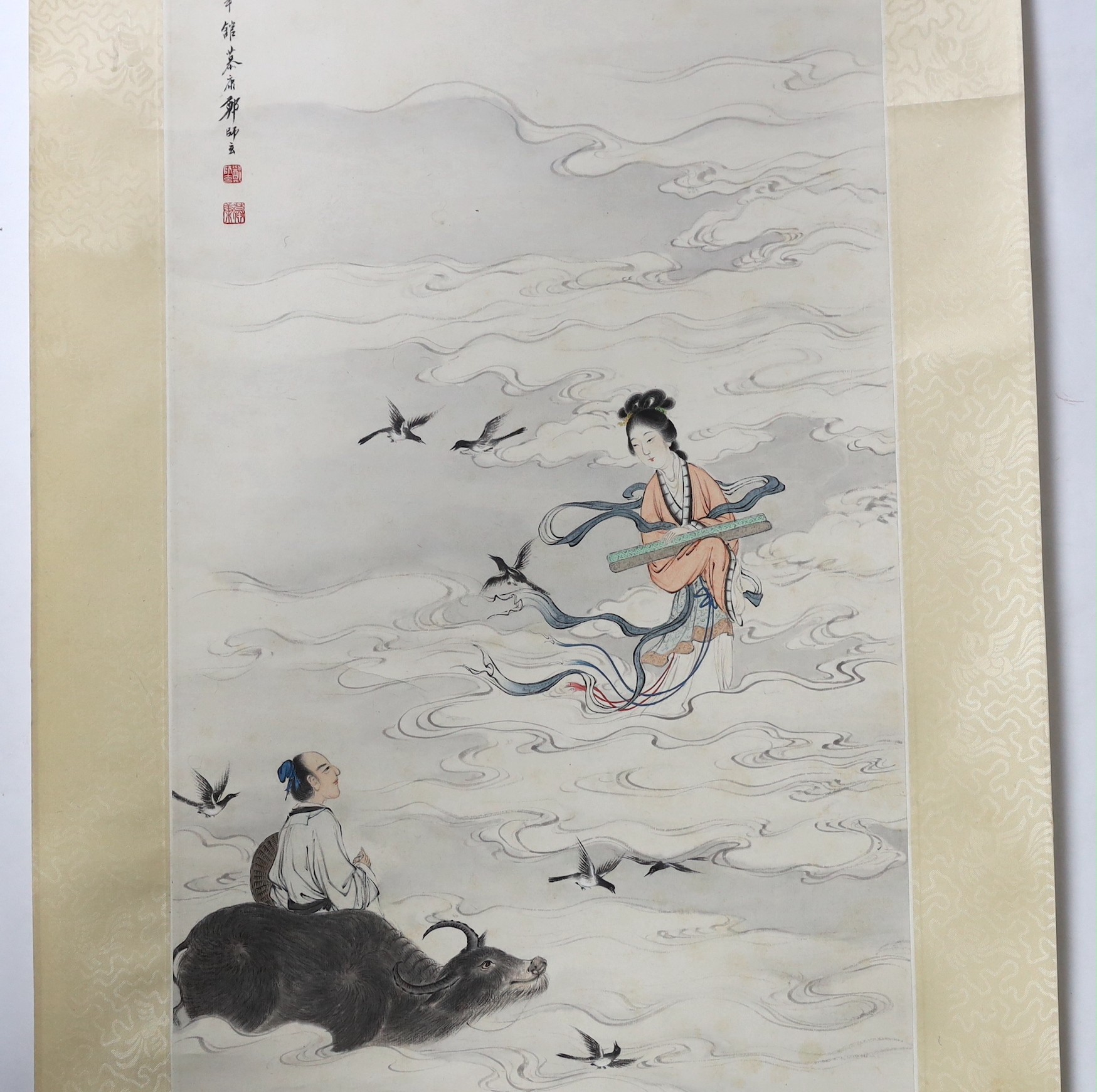 A Chinese scroll painting on paper of a female immortal and a male immortal riding a Buffalo amid clouds and birds, early 20th century, image 77cm x 34.5cm